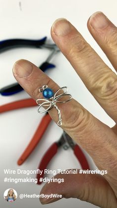 a hand holding a wire wrapped ring with blue beads on it and some scissors in the background