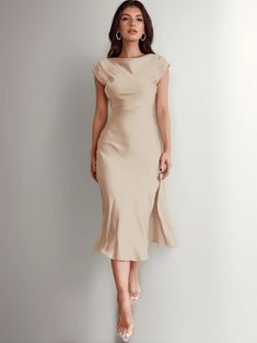 a woman in a beige dress standing against a wall