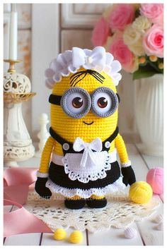 a crocheted minion is sitting on a doily with flowers in the background