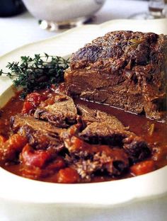 a white plate topped with meat and tomato sauce next to a bowl of soup on top of a table