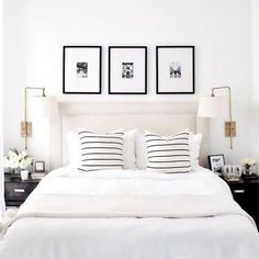 a white bed with three framed pictures on the wall above it and two nightstands