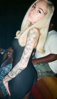 a woman with long blonde hair and tattoos on her arm is posing for the camera