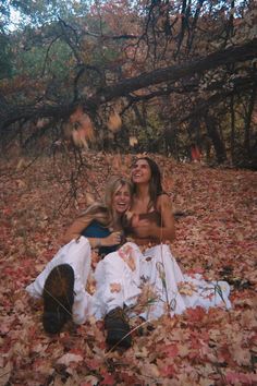 two women are sitting on the ground covered in leaves and looking up into the sky