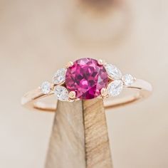 a close up of a ring with a pink stone in the middle and two white diamonds on it