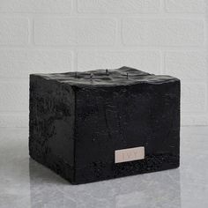 a black box sitting on top of a table next to a white brick wall with a name plate