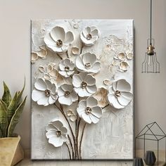 an abstract painting with white flowers on a gray wall next to a potted plant