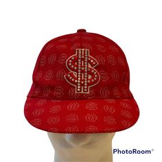 a red baseball cap with a dollar sign on the front and diamond embellishments