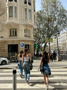 two women walking across a cross walk in front of a tall building with many windows