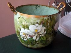 a green bowl with white flowers painted on the side and gold handles sitting on a table