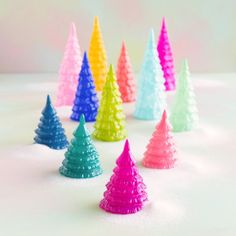 there are many small plastic christmas trees on the white counter top, all in different colors