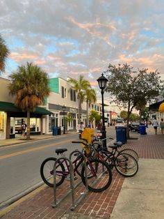 three bikes are parked on the sidewalk in front of buildings and palm trees at sunset