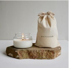 a small candle sitting next to a bag on top of a stone slab with the word post botanical written on it