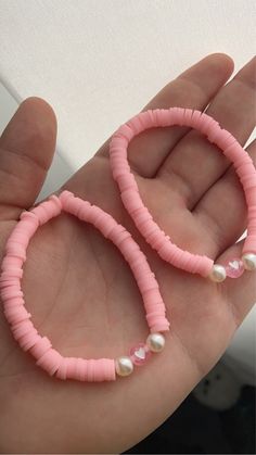 a hand holding two pink bracelets with pearls