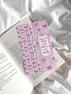 two pink bookmarks sitting on top of a white bed next to an open book