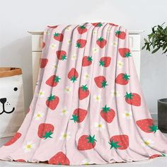 a pink blanket with strawberries on it next to a potted plant and a teddy bear