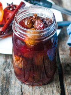 a jar filled with jelly sitting on top of a wooden table next to sliced fruit