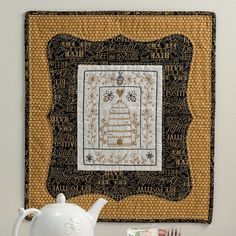 a white tea pot sitting on top of a wooden table next to a wall hanging