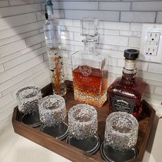 four glasses are sitting on a tray with liquor bottles in front of the glass jars