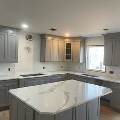 an empty kitchen with marble counter tops and gray cabinets