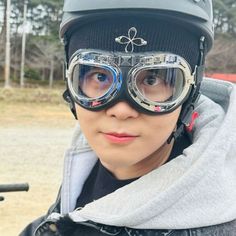 a young boy wearing goggles and a hat on top of his head while standing next to a motorcycle