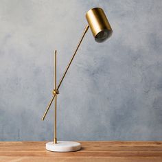 a gold desk lamp on top of a wooden table next to a gray wall and floor