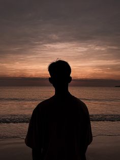 a man standing on top of a sandy beach next to the ocean at sunset or dawn