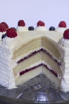 a cake with white frosting and raspberries is cut in half to show the layers