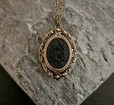 A detailed black on black rose cameo set in detailed antiqued brass, on an antiqued brass locket.  Chain is antiqued brass.  Locket opens with two spaces. Details: Locket measures 1.25 inch x 7/8 inch Chain measures 18 inches Locket and chain are plated brass Back of locket is engraved as shown Cameo is hard, matte resin Lead and nickel free Please allow for possible slight color differences due to different settings on different screens. Thank you for shopping Delicate Industry :) Bronze Gothic Jewelry For Gift, Gothic Brass Jewelry Gift, Vintage Black Jewelry With Antique Finish, Vintage Black Locket Jewelry, Antique Black Brass Necklace, Vintage Black Locket Necklace, Collectible Black Locket Jewelry, Vintage Black Brass Jewelry, Black Vintage Brass Jewelry