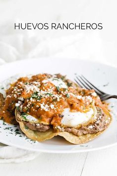 a white plate topped with pancakes covered in cheese and sauce next to a fork on top of it