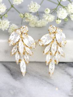 two pairs of gold tone earrings with clear crystal stones and leaves, on top of a marble