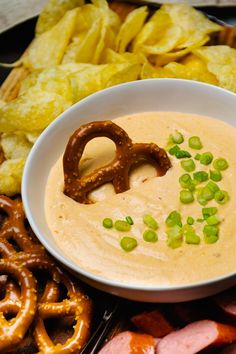 a white bowl filled with dip surrounded by pretzels, chips and crackers