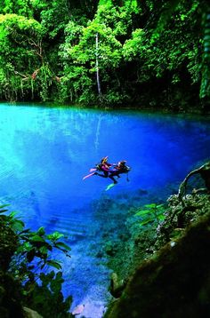 a person floating in the middle of a lake surrounded by trees and rocks with blue water