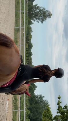 there is a woman riding a horse on the field with trees in the back ground