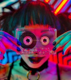 a woman holding up a cassette in front of her face with two eyeballs on it