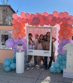 a group of people standing in front of a pink and blue arch with balloons on it