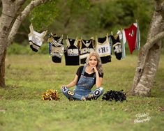 a woman sitting in the grass next to some clothes hanging on a line and trees