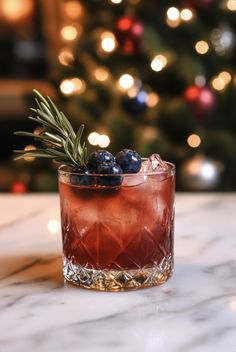 a drink with blueberries and rosemary garnish in front of a christmas tree