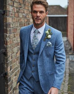 a man in a blue suit and flowered boutonniere standing next to a brick wall