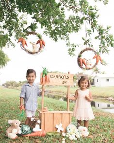 two young children standing next to each other in the grass with carrots on display