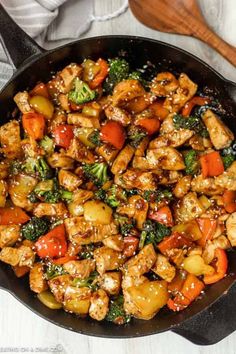 a skillet filled with chicken and vegetables on top of a white table next to a wooden spoon