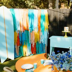 an orange table with plates and cups on it in front of a colorful wall decoration