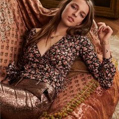 a beautiful woman laying on top of a couch next to a brown pillow and gold purse