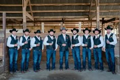 a group of men standing next to each other wearing cowboy hats and vests in a barn