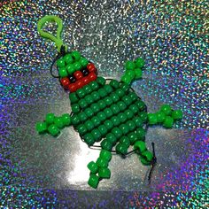 a green frog ornament made out of legos sitting on a shiny surface