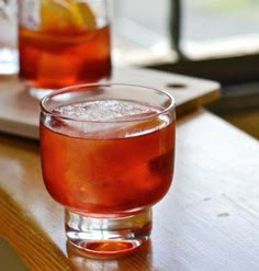 two glasses filled with drinks sitting on top of a wooden table