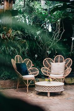 two wicker chairs sitting next to each other on a brick patio surrounded by greenery