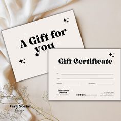 two gift certificates sitting next to each other on top of a white cloth covered table