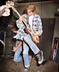 two young men are playing guitars in a recording studio, one is jumping and the other is standing