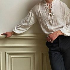 a man is leaning against a wall with his hands on his hips, wearing a white shirt and black pants