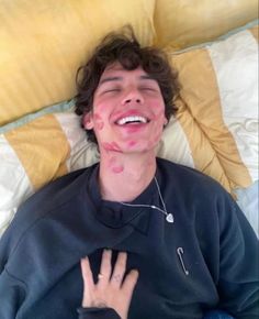 a young man laying on top of a bed covered in yellow and white sheets smiling